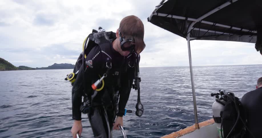 A man wearing full scuba gear climbs out of a body of water into a boat with other people