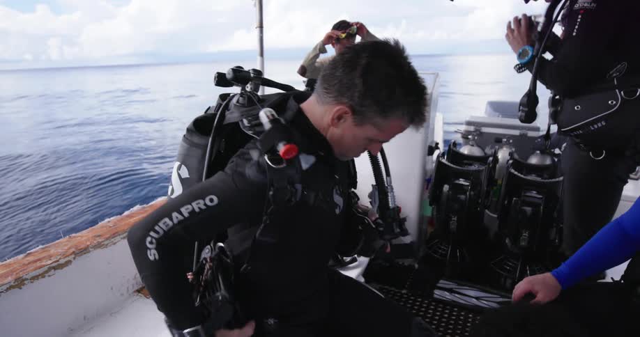 Several men on a boat put on diving equipment as another man drives the boat