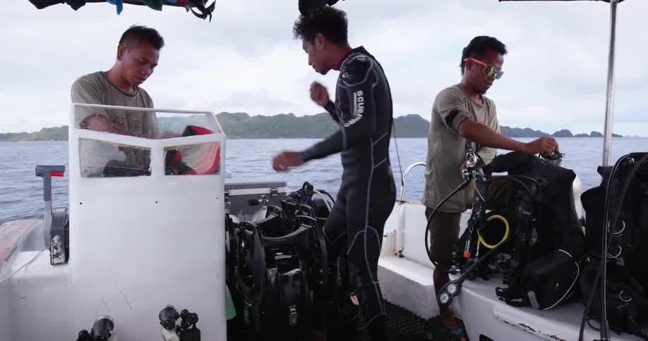 Three men on boat examine scuba gear with misty island on horizon
