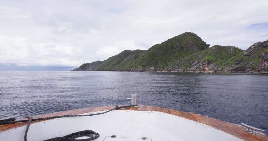 A boat floating on an ocean just off an island in the daytime