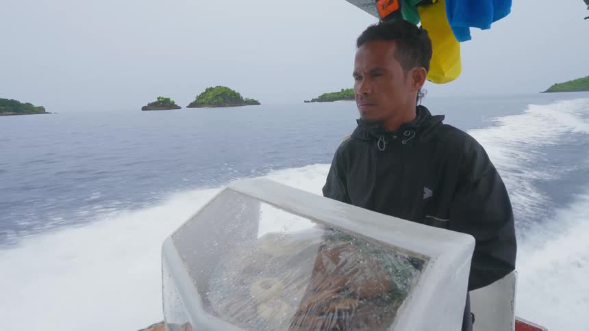 A man quickly steers a speedboat in the ocean as another man behind him waves frantically