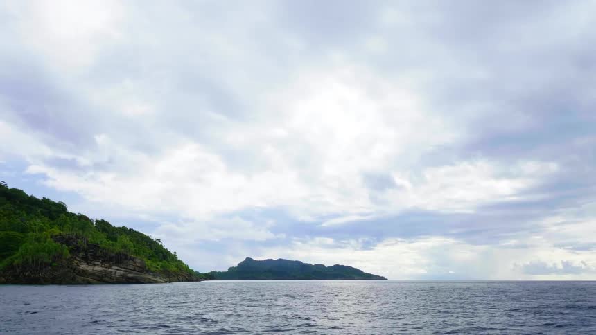 Small waves move around a promontory covered in lush green trees