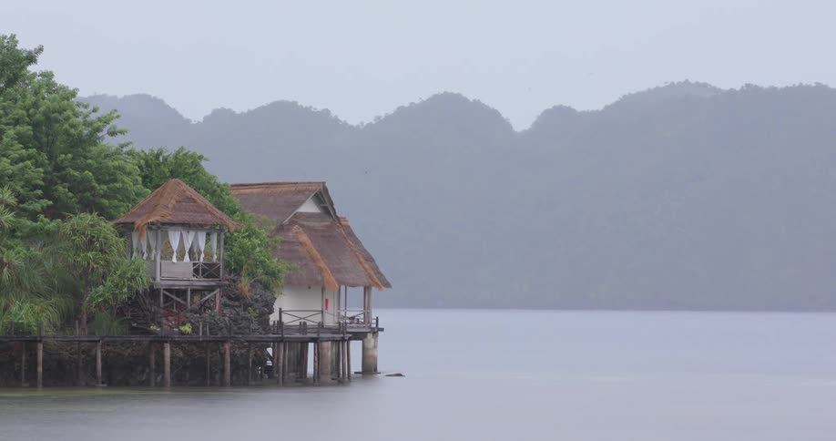 Rain pours near a waterfront house around midday in a bay