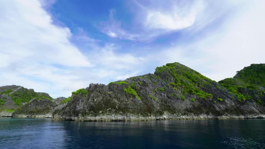 A coastal land with plants with a body of water in the foreground and the sky and clouds in the background