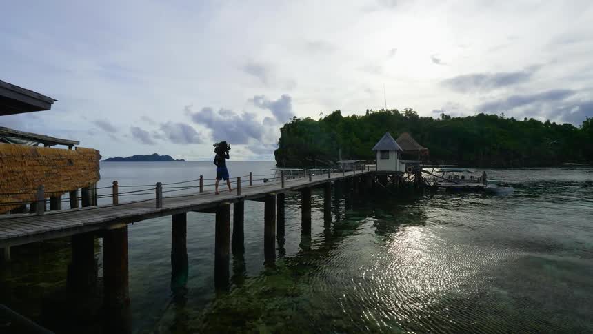 A person carries something on their shoulder walking across a lake pier