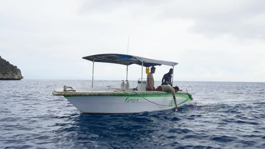 Multiple people in a boat lean over the edge to someone on the water