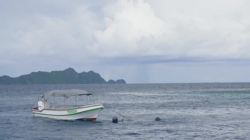 A small pontoon boat is anchored in the ocean