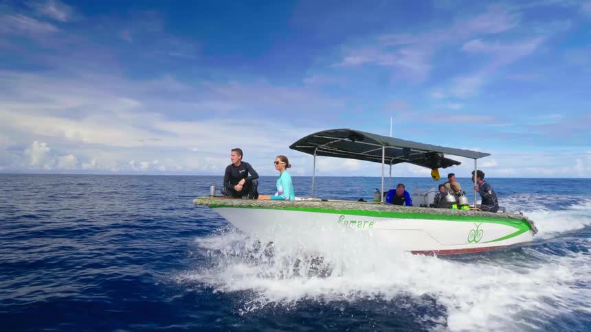 Men and women are riding on a motor boat in a body of water with scuba gear visible