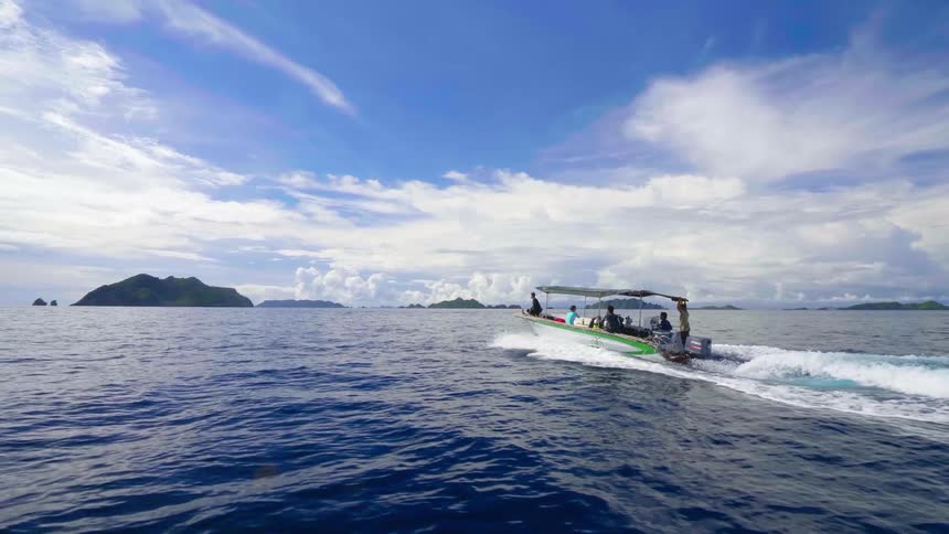 A boat carries a group of people across the ocean on a sunny day
