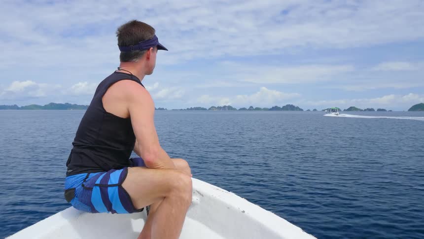 A male sitting on the edge of a moving boat traveling on a lake