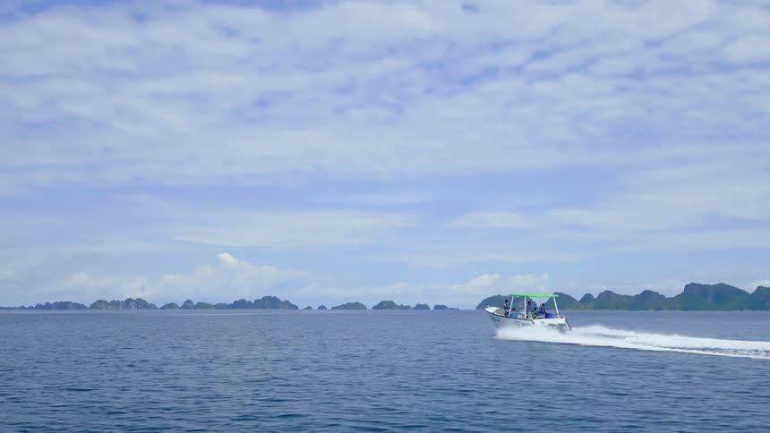 A group of people travel across the ocean towards islets in the distance on a boat during the day