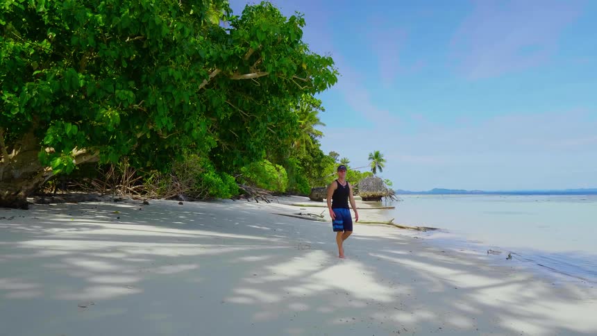 A man walks along a sandy beach on a sunny day