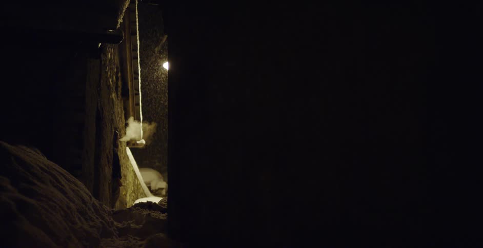 Snow falling as a person stands outside and smokes next to a snowbank