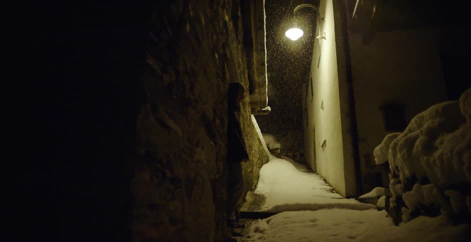 A man smoking outdoors on a sidewalk covered in snow at night