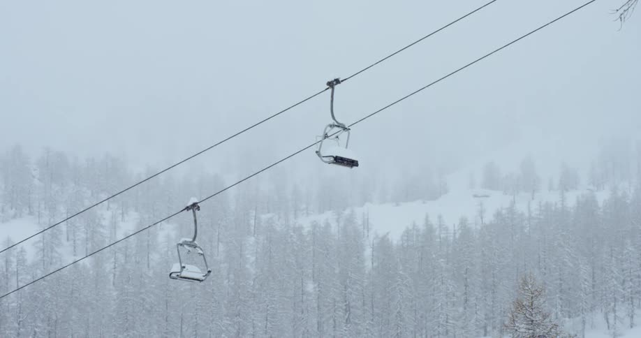 Snow falling over a forest and ski chair lift on a hill