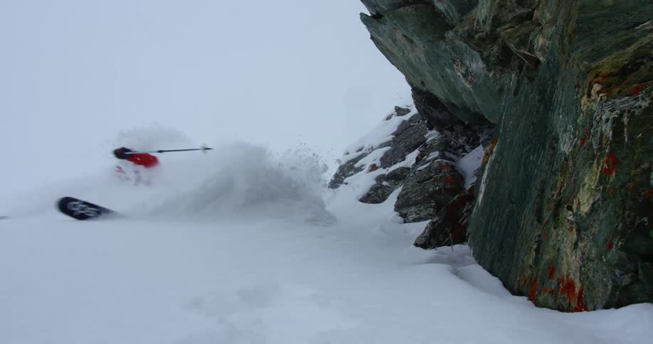 Snow flies up in the air as a person skis down a mountain