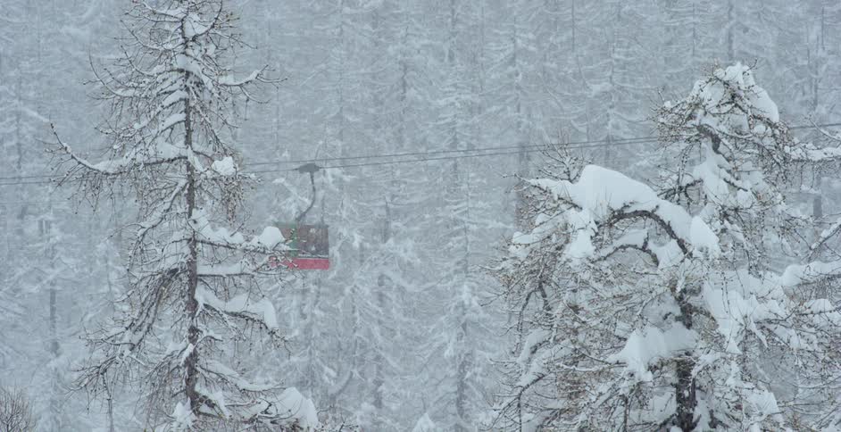 A ski lift moves slowly past a forest as heavy snow falls
