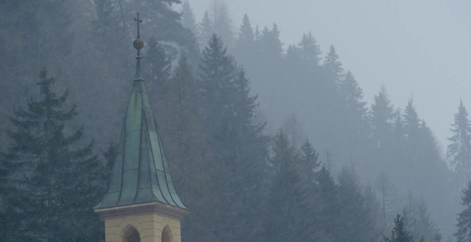 Snow falling around a church steeple in a pine forest in winter