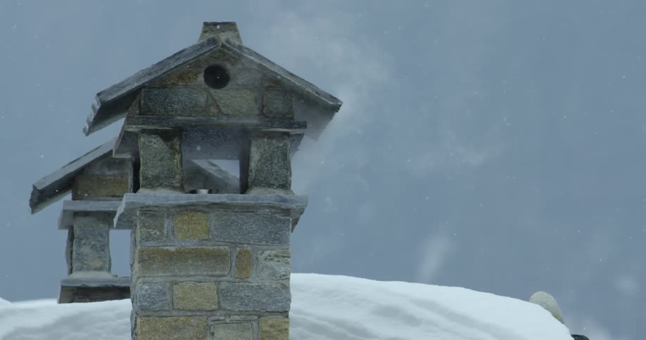 Smoke rises from chimneys of stone walled buildings as it snows