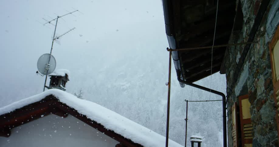 Snow falling around buildings in a mountain forest