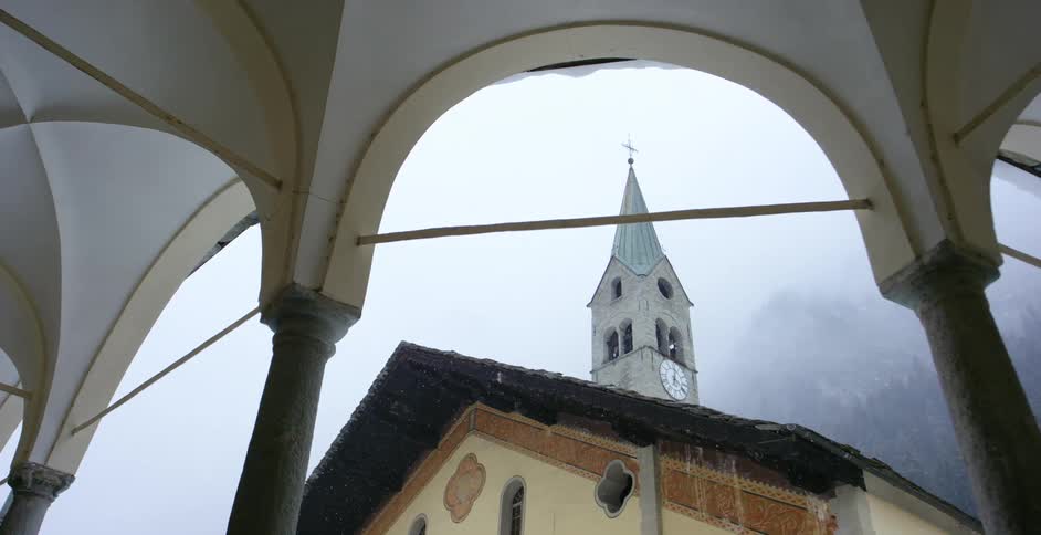 A steeple atop a church next to a foggy mountain covered in forest during the day