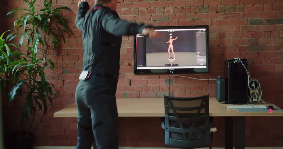 Man balances in room capturing his motion and displaying it on screen hanging on brick wall