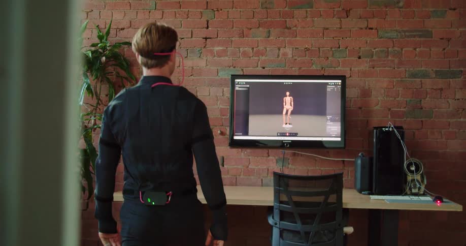 A man is exercising indoors with a device attached to his head that is transferring his movements to a monitor on the wall