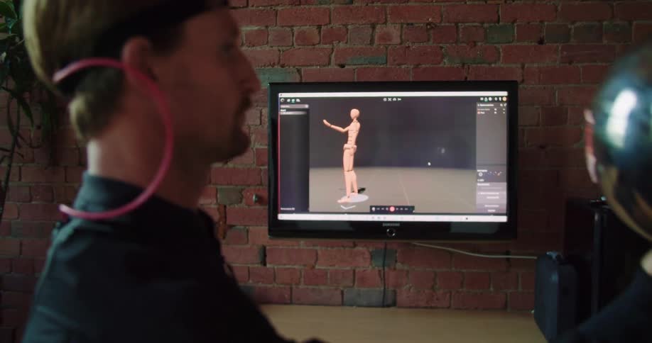 A man with a virtual reality suit and a silver ball looking at a monitor on the wall