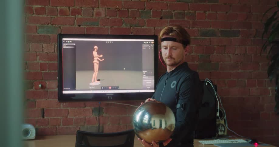A man watches a screen and mimics a robot as he plays a virtual game