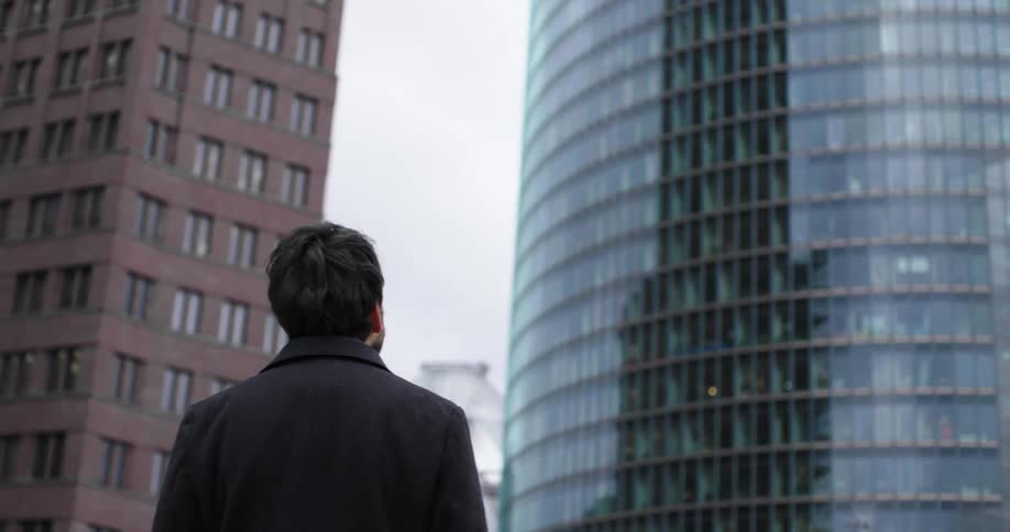 A man looks up in awe at high rise apartment buildings in a city