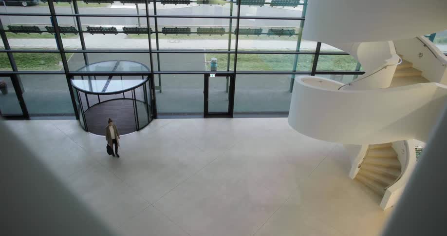A woman walks into a modern office building with a spacious foyer and curved staircase