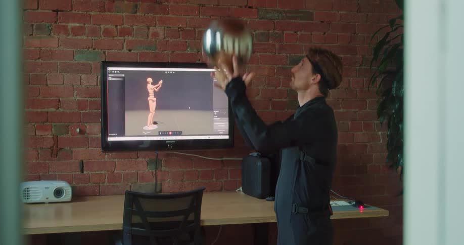 Man throws ball to capture motion shown on screen hung on brick wall