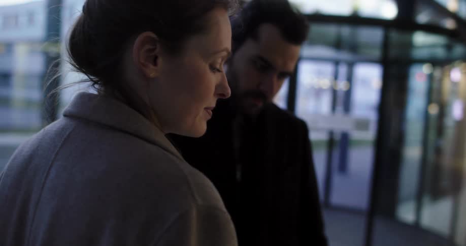 A woman holding a smart phone and standing in a building next to a man