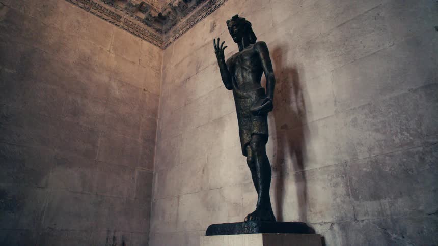 A tall statue of a man stands atop a pedestal where it casts a shadow on the wall