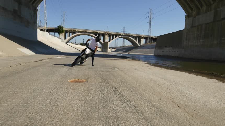 A person rides a dirt bike in circles doing donuts on a bypass road by a bridge