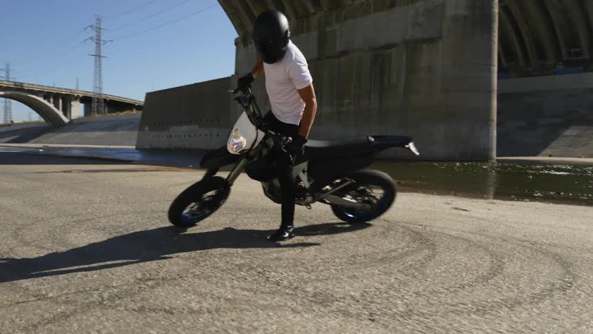 A man with a helmet on a motorcycle with a bridge the sky and clouds in the background