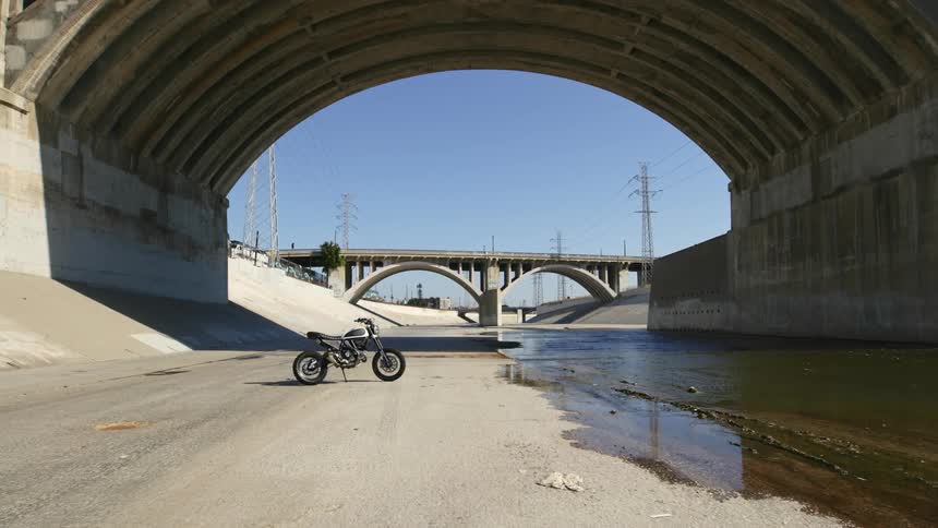A motorcycle parked beneath a bridge on a flood control channel on a sunny day