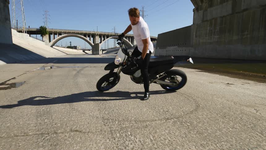 A man does donuts on a dirt bike in a bypass area with no vehicles