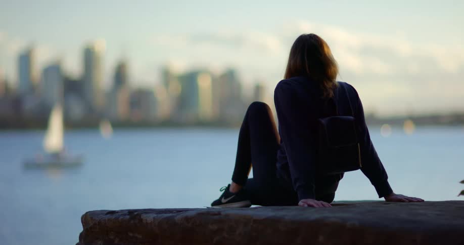 A young woman sits on the shore and watches the sailboats in the water