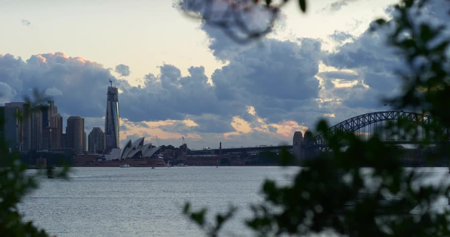 A body of water with a bridge an opera house buildings and the sky and clouds in the background