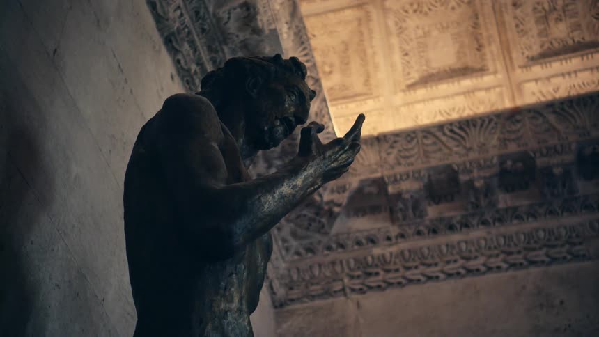 Bronze statue of barechested man with ornate detailed ceiling above and tiles behind