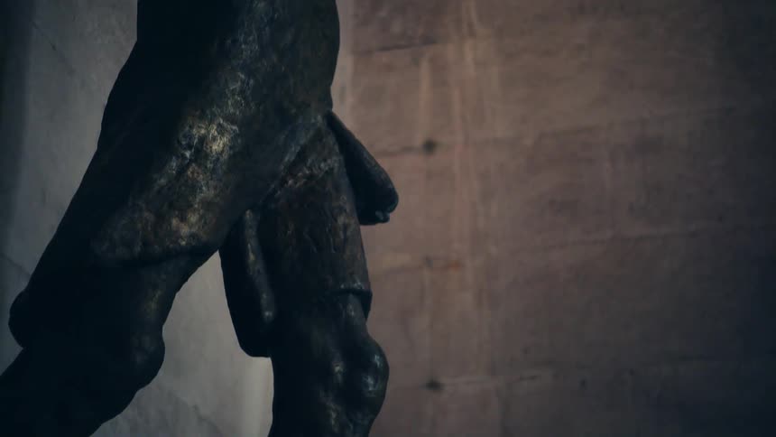 Bronze sculpture stands on pedestal under ornate detailed ceiling