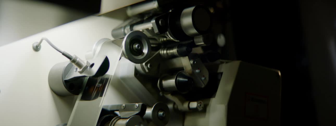Pieces on a movie projector spin and turn in a theater