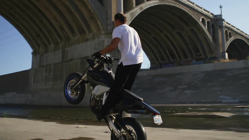 A man driving down a street on his motorcycle pops a wheelie and drives on one wheel
