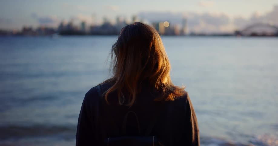 A woman is standing by the ocean at dusk