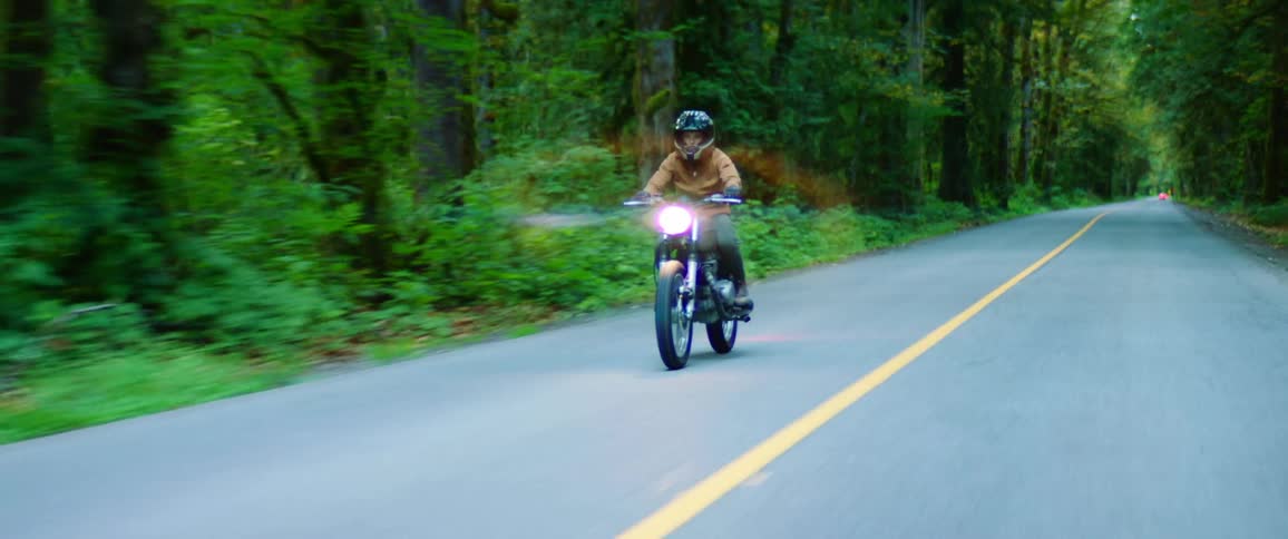 A motorcyclist rides a motorcycle on a road through a forest during the day