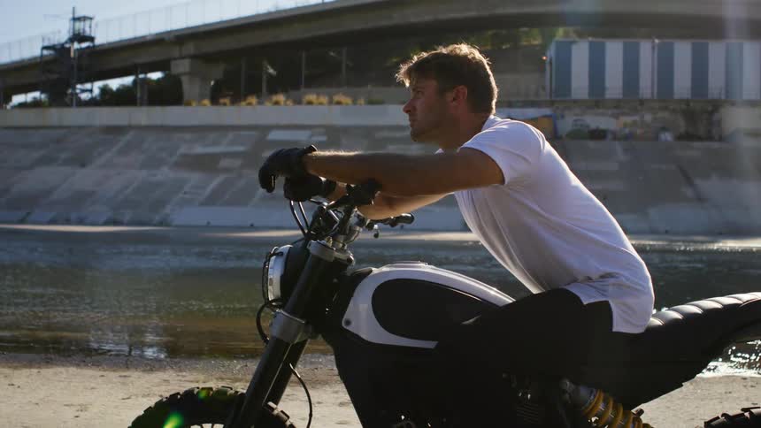 A man is sitting on his parked motorcycle outdoors