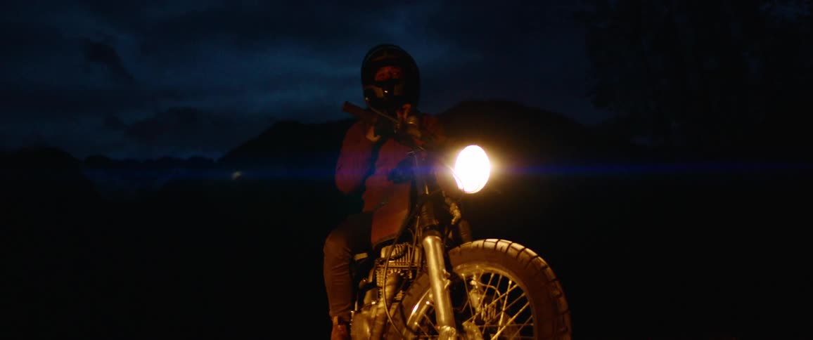 A woman sitting on an idle motorcycle puts on her helmet at night