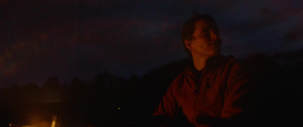 Person sits on motorcycle with lit lights at night backed by mountains
