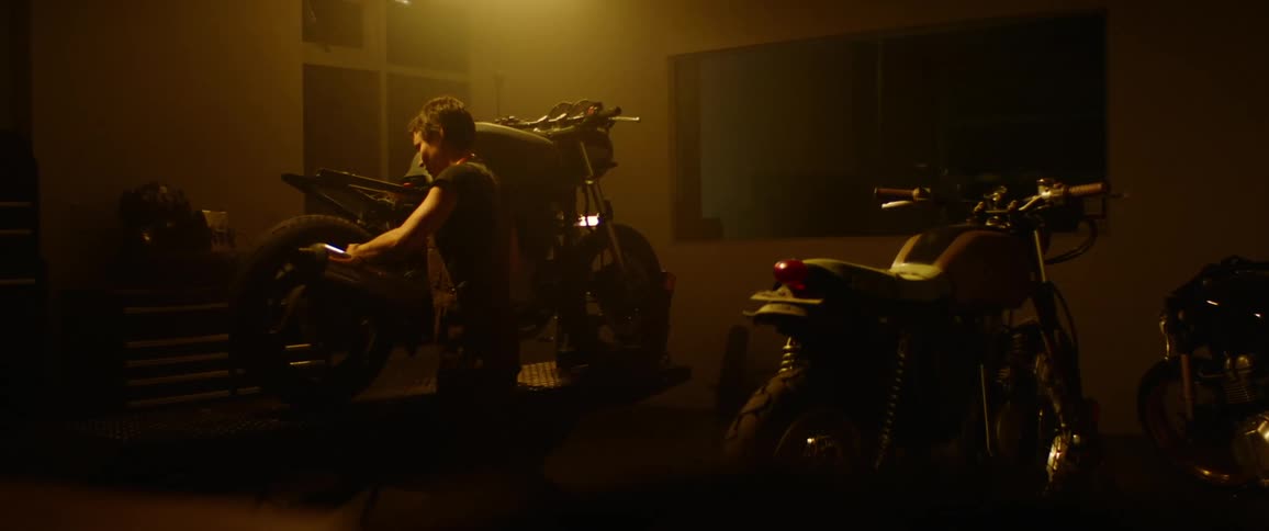 A woman works on the rear wheel of a motorcycle in a dimly lit garage